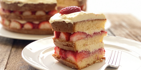 A slice of layered strawberry cake on a plate with a fork