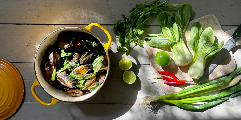 Pots of mussels next to a chopping board and Asian vegetables.