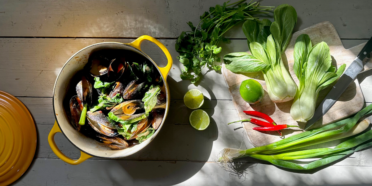 Pots of mussels next to a chopping board and Asian vegetables.